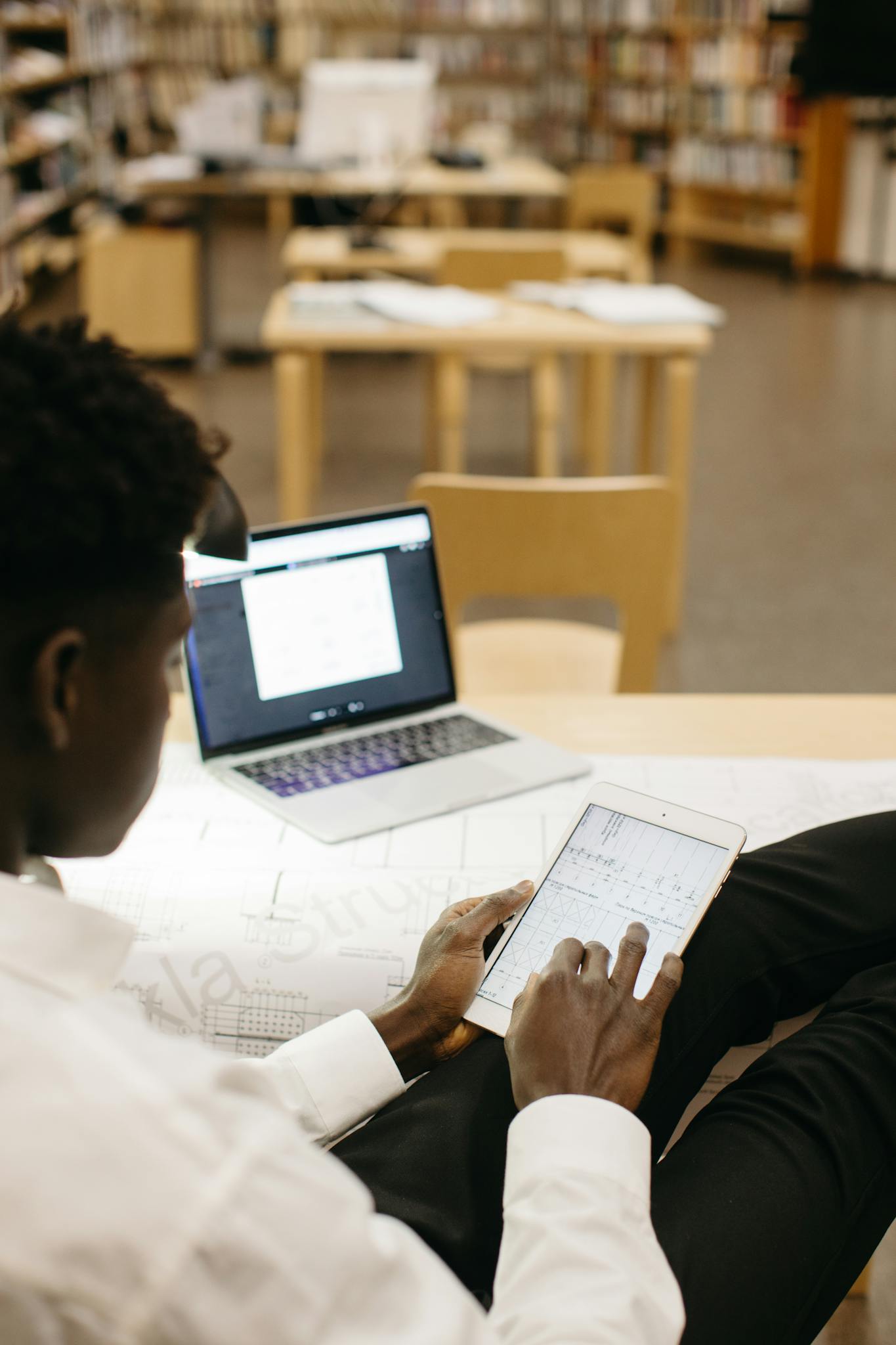Architect reviewing blueprints on a digital tablet in a library setting.