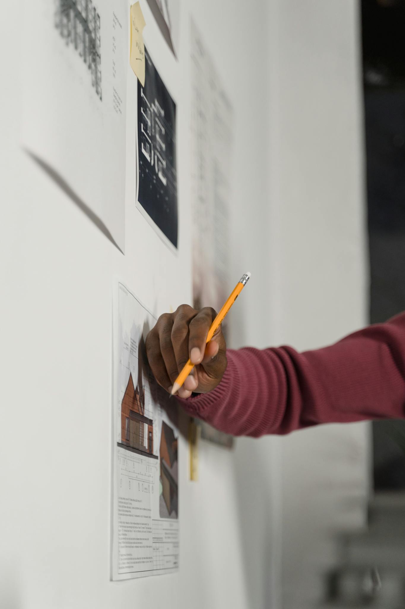 Close-up of a hand holding a pencil sketching architectural plans on a wall-mounted board.